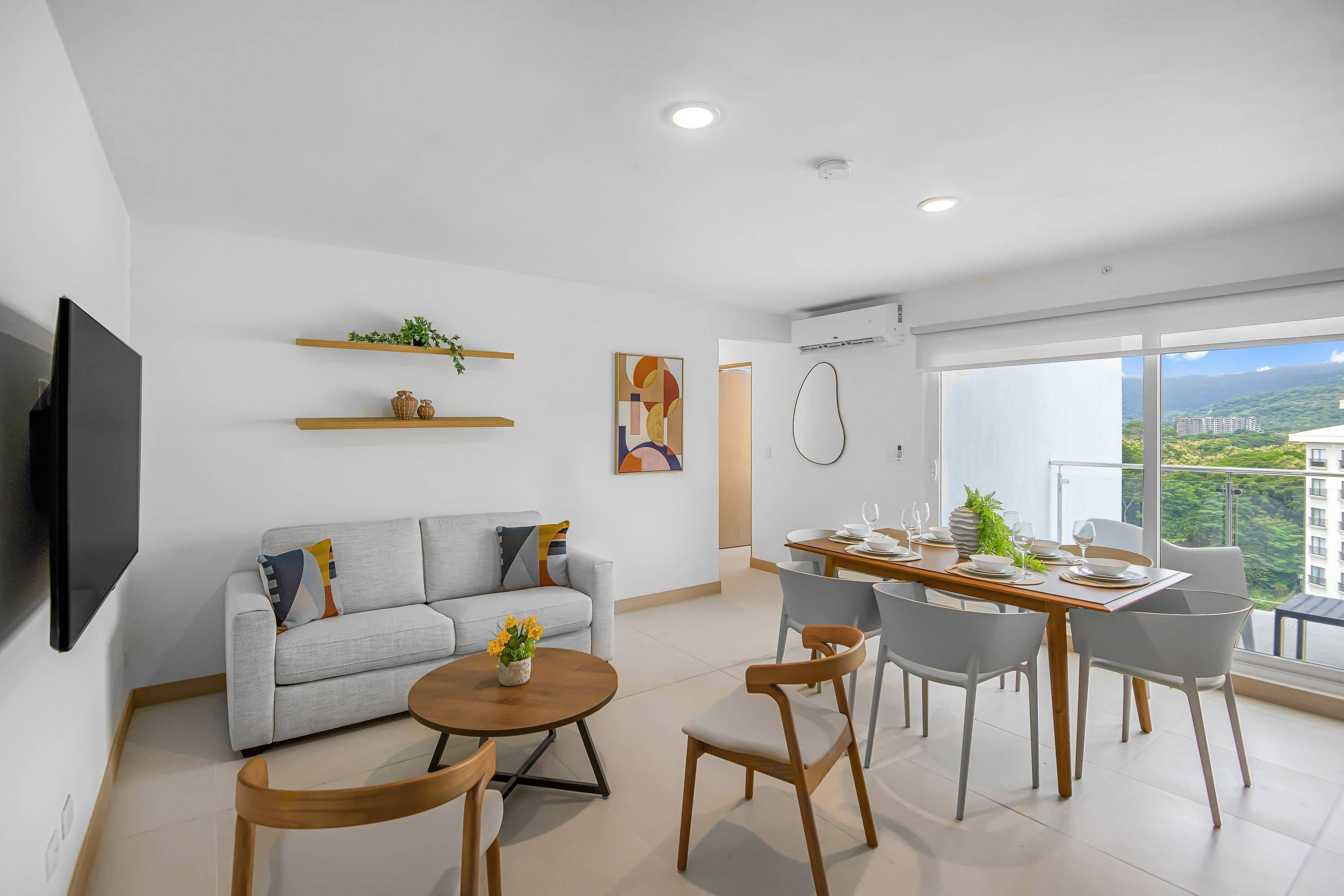 Ein modernes Wohnzimmer mit einer Couch, einem Esstisch, Stühlen und einem Fernseher. Regale mit Pflanzen und ein Gemälde an der Wand.