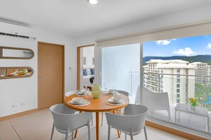 Ein moderner Essbereich mit einem runden Tisch für vier Personen, weißen Stühlen und Blick auf eine Stadtkulisse durch große Fenster.