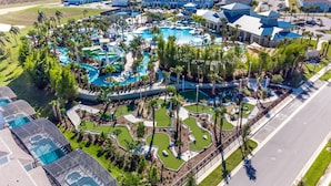 An aerial view of a resort with multiple swimming pools, palm trees, and a golf course. - Upstay - Disney Movie Mansion at Windsor Island (Clermont)