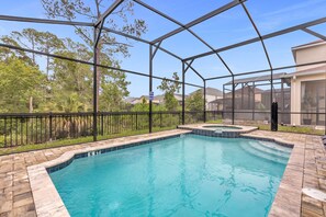 A swimming pool with a glass enclosure, surrounded by a stone deck and a black metal fence.