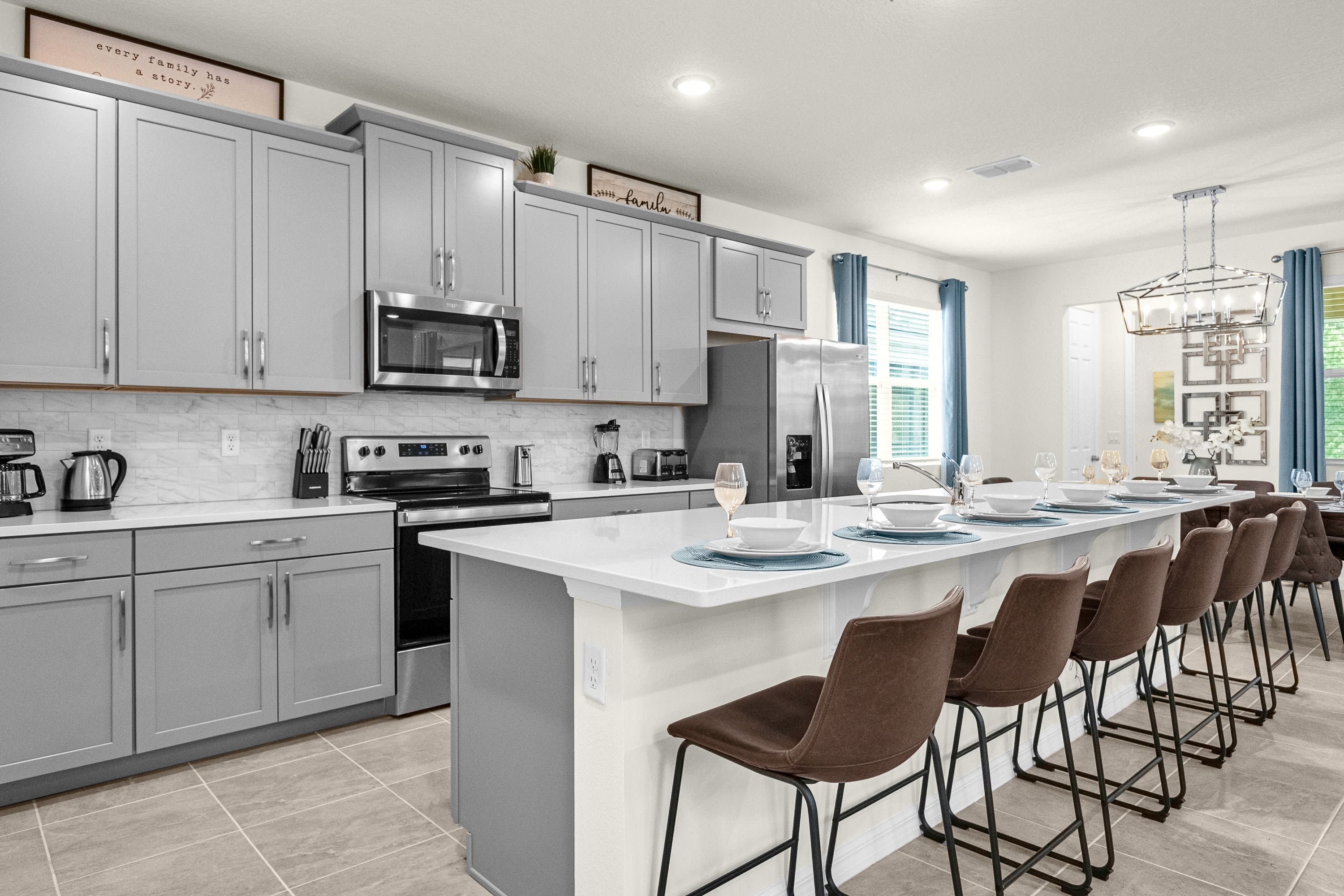 A modern kitchen with grey cabinets, a large island with bar stools, stainless steel appliances, and a view of the dining area.