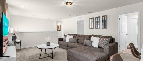 A modern living room with a sectional sofa, a round coffee table, and a flat-screen TV.