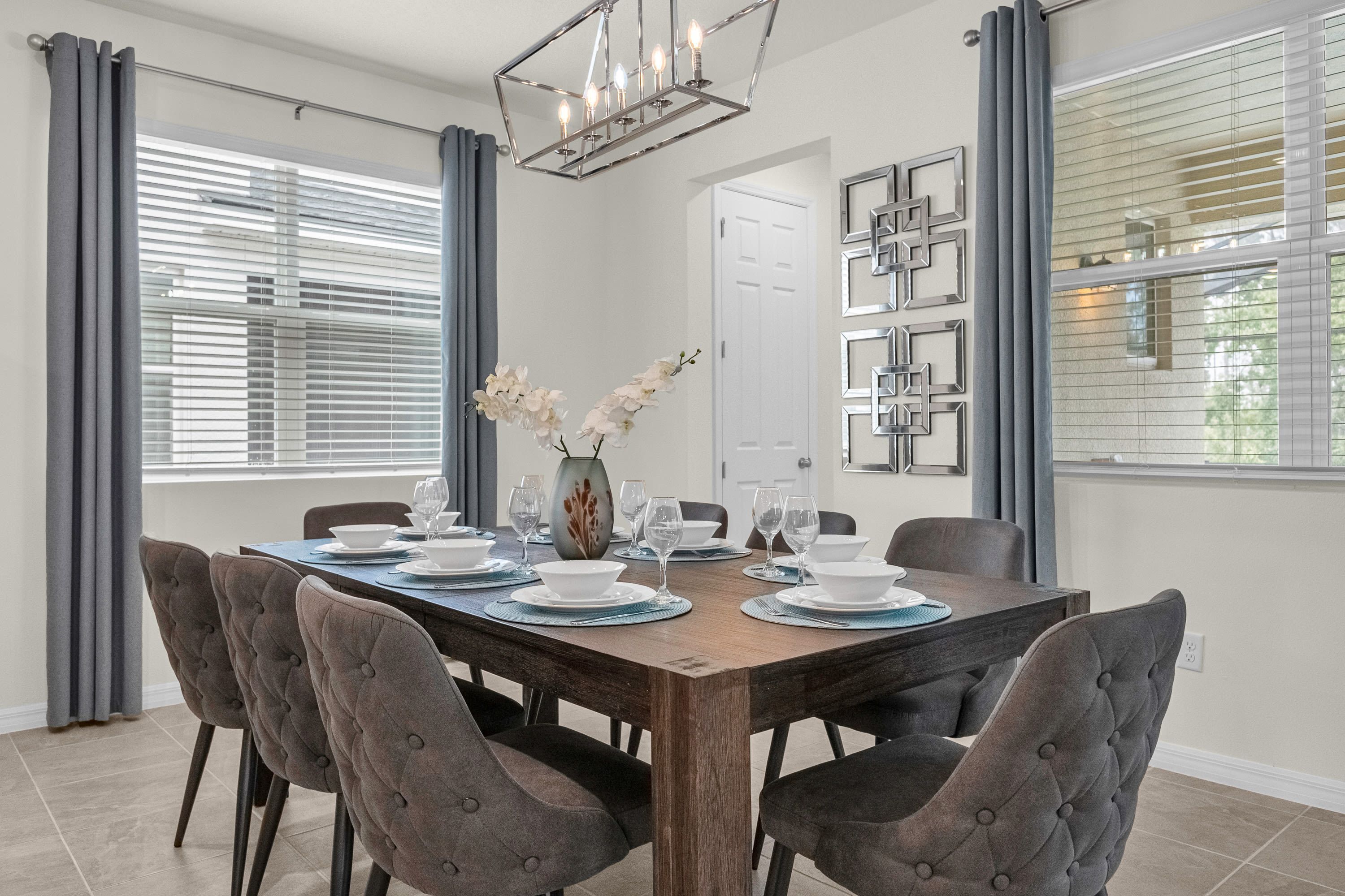A dining area with a wooden table set for six, surrounded by tufted chairs.