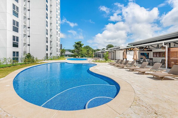 Relax by the large, curved pool surrounded by a patio area with lounge chairs and umbrellas.