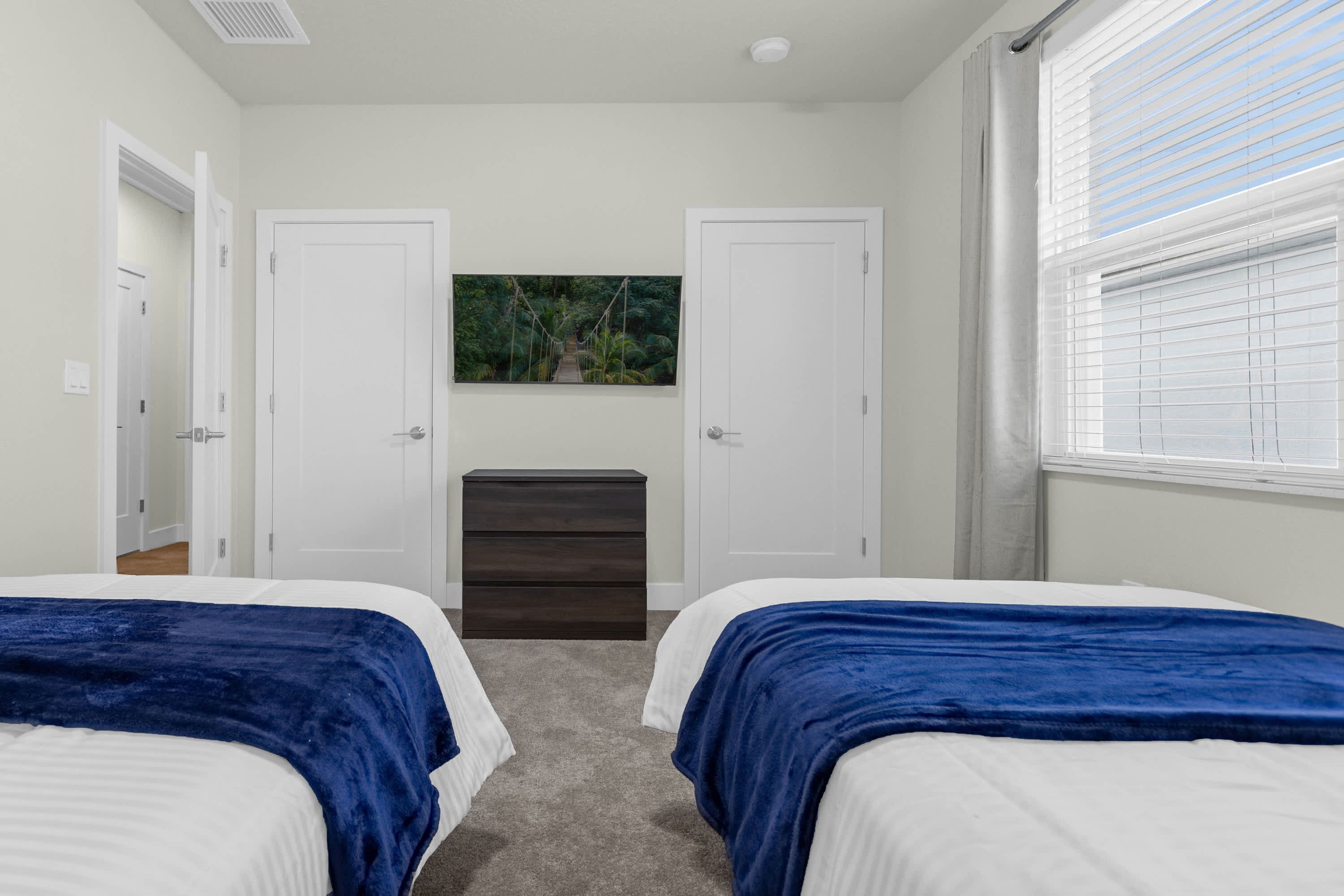 A bedroom with two beds, a dresser, and a window with blinds.