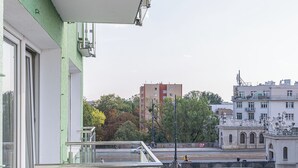 Vista desde un balcón con barandilla de vidrio, que da a una calle con un puente, edificios y árboles.