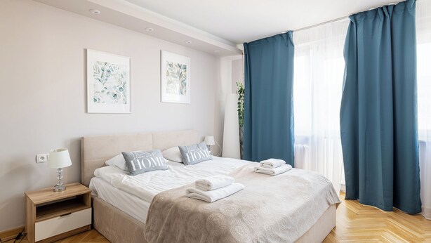 Una cama bien hecha con colcha color beige y dos almohadas, una mesita de noche con lámpara, y un cuadro en la pared.