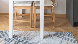 Un comedor con una mesa y sillas de madera, un cuadro en la pared, un reloj y una pequeña estantería con flores.