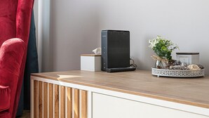 Una habitación moderna con un escritorio de madera, una silla roja, un altavoz pequeño y un jarrón decorativo con flores.
