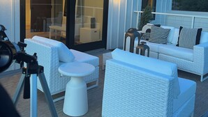 A rooftop patio with white wicker furniture, a telescope, and a glass door leading to an indoor area.