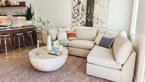 A modern living room with a sectional sofa, a round coffee table, and a kitchen area with bar stools.