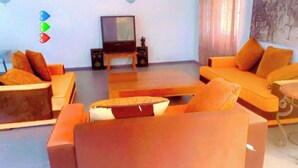 Un soggiorno con divani arancioni, un tavolino in legno, una televisione e degli altoparlanti.