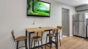 Eine moderne Küche mit integriertem Kühlschrank, einem Holztisch mit vier Stühlen und einem an der Wand befestigten Flachbildfernseher, der eine Naturansicht zeigt.