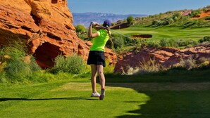 A golfer on a green with a rocky cliff in the background.