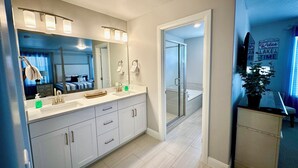 A modern bathroom with a large mirror, white cabinets, a sink, and a shower area.