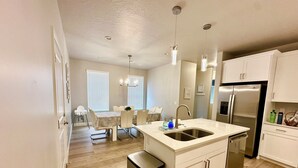 A modern kitchen with a central island, stainless steel appliances, and a dining area with a white table and chairs.