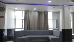A modern hotel lobby with a curved grey sofa, large windows with curtains, and a "Fire Exit" sign. - HOTEL LAXMI PALACE (Kekri)
