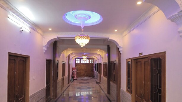 A hallway with a chandelier, wooden doors, and a patterned floor. - HOTEL LAXMI PALACE (Kekri)