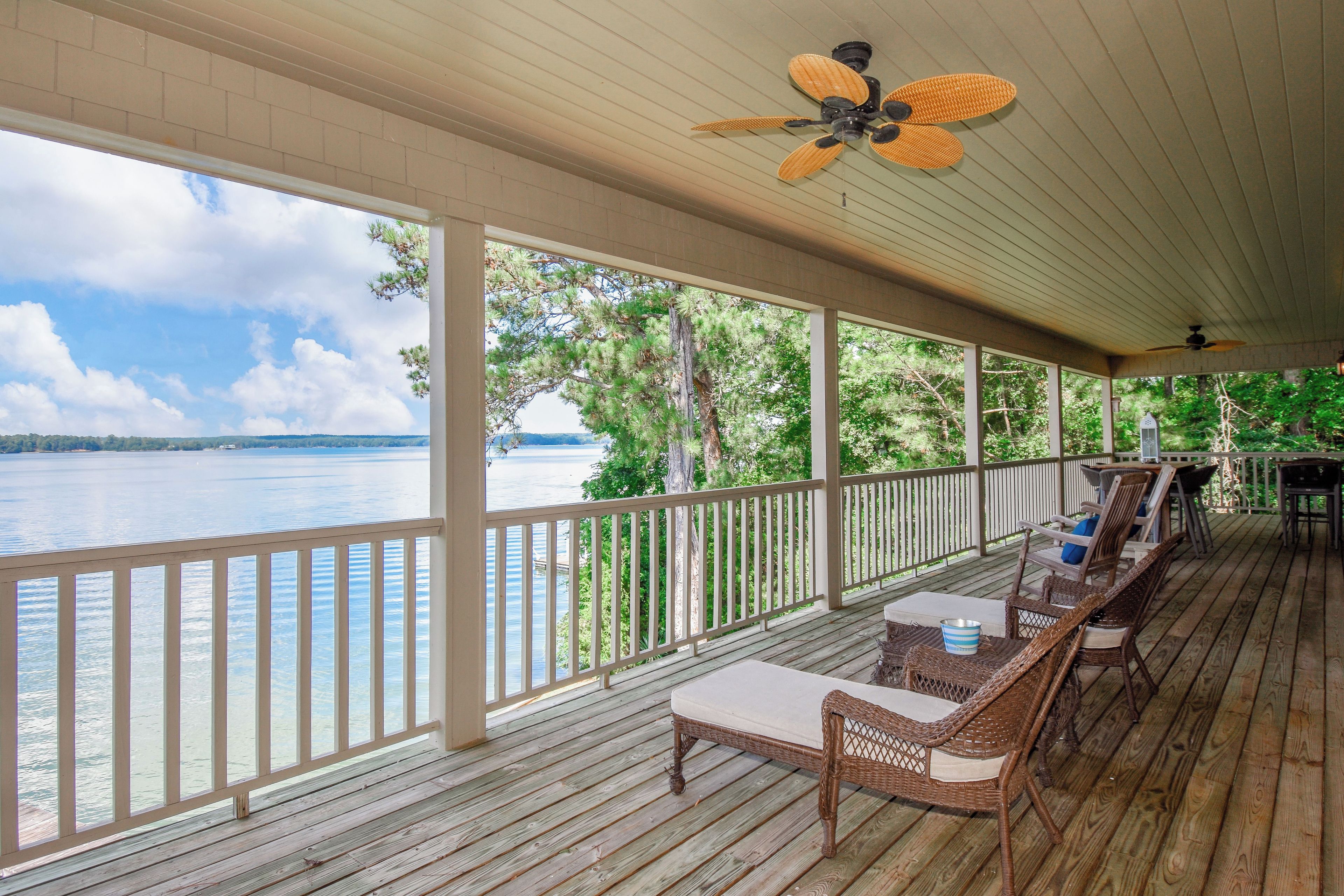 A covered deck with wicker furniture, a view of a lake, and ceiling fans.