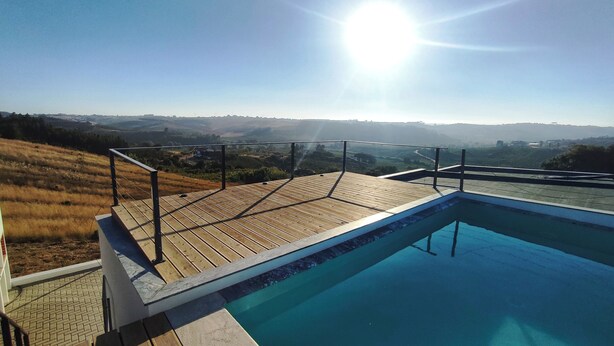 A swimming pool with a wooden deck and metal railing, surrounded by a scenic landscape. - Nature, Naturally... (Cadaval)