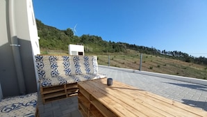 A wooden deck with a bench and a table, overlooking a hilly landscape with a wind turbine. - Nature, Naturally... (Cadaval)