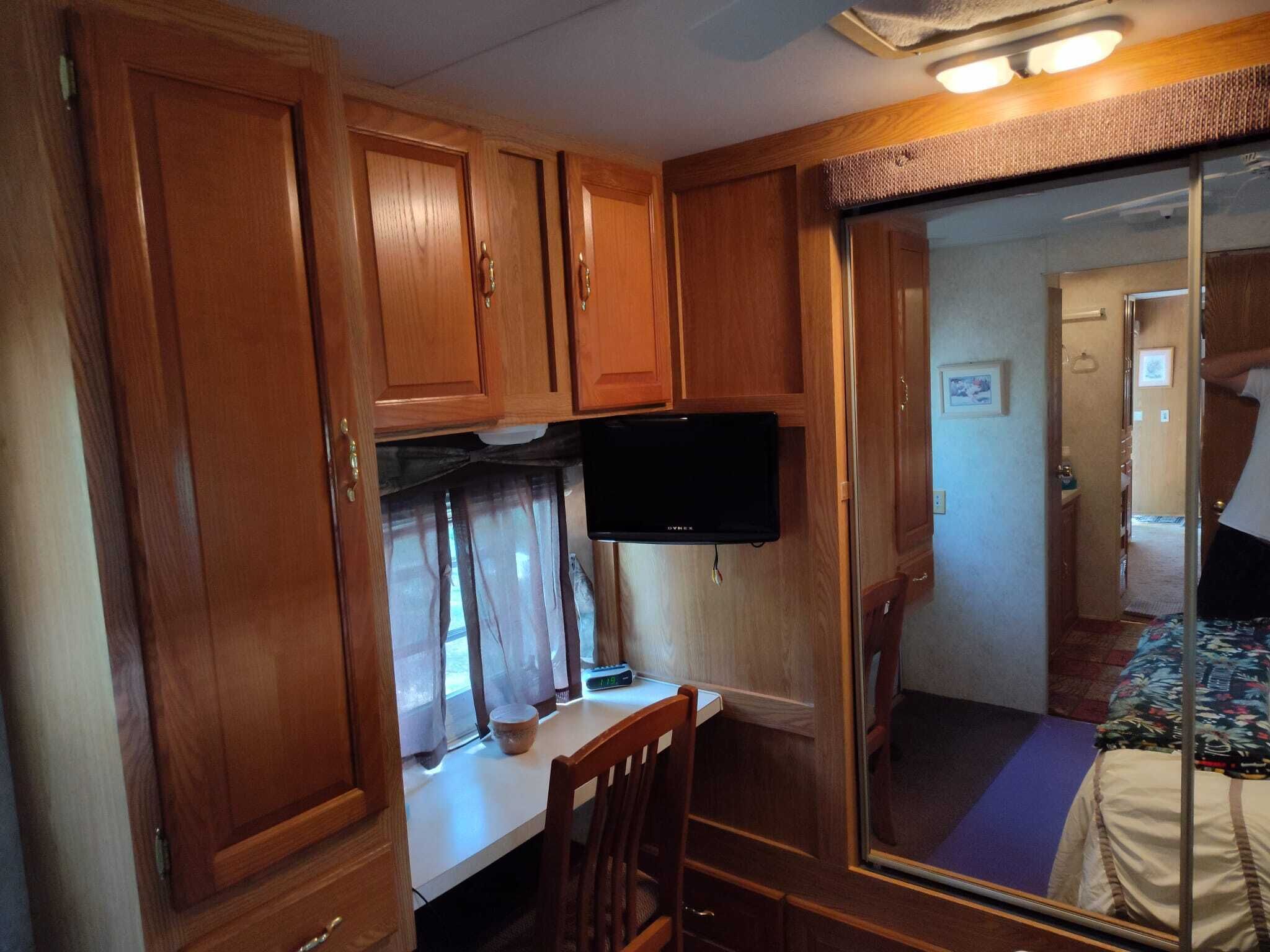 A compact RV interior with wooden cabinetry, a mounted television, a small table, and a bed.