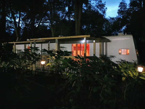 A modern, single-story structure with a glass enclosure, surrounded by dense foliage and illuminated by ambient lighting.