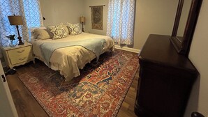 Un dormitorio con cama, mesitas de noche, cómoda, ventilador de techo y cortinas estampadas.