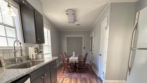 Una cocina con encimeras de granito, lavavajillas, zona de comedor con mesa y sillas, y alfombra estampada.
