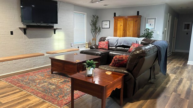 Un salón con sofá de cuero, mesa de centro de madera y televisor montado en la pared.