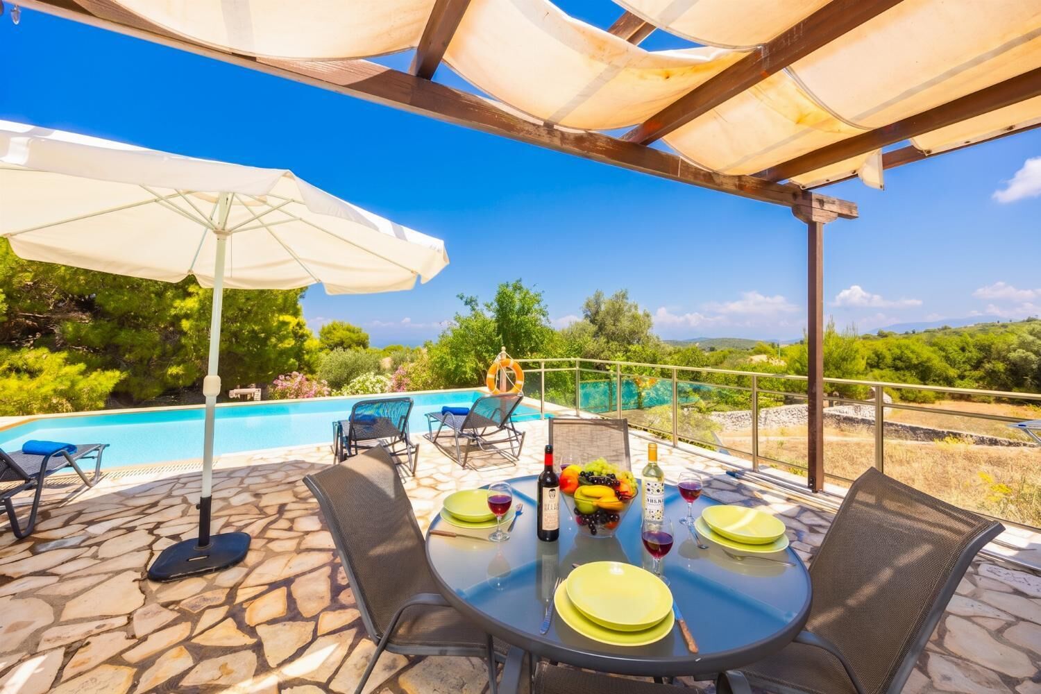 An outdoor dining area with a pool, stone flooring, and a view of the landscape.