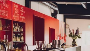 Una zona de bar con taburetes y una barra que exhibe distintas botellas y copas.