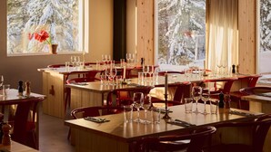 Un restaurante con varias mesas y sillas, ventanas amplias que dan a árboles cubiertos de nieve.
