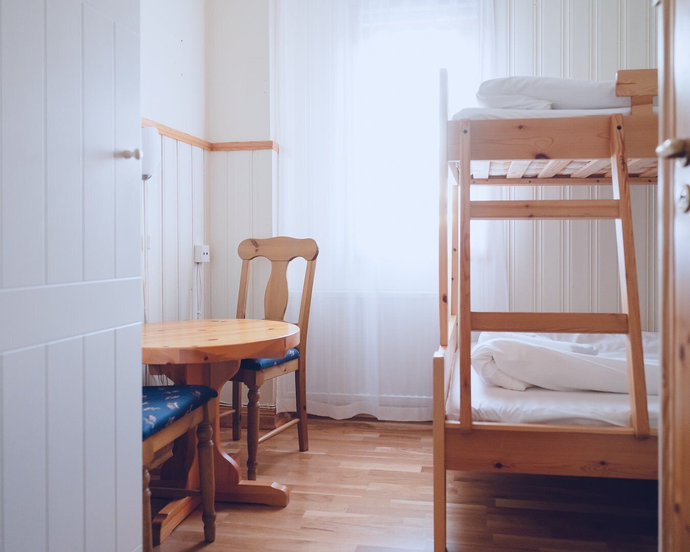 A bunk bed with a wooden frame, a wooden chair with a cushion, and a small wooden table with a blue cushion.