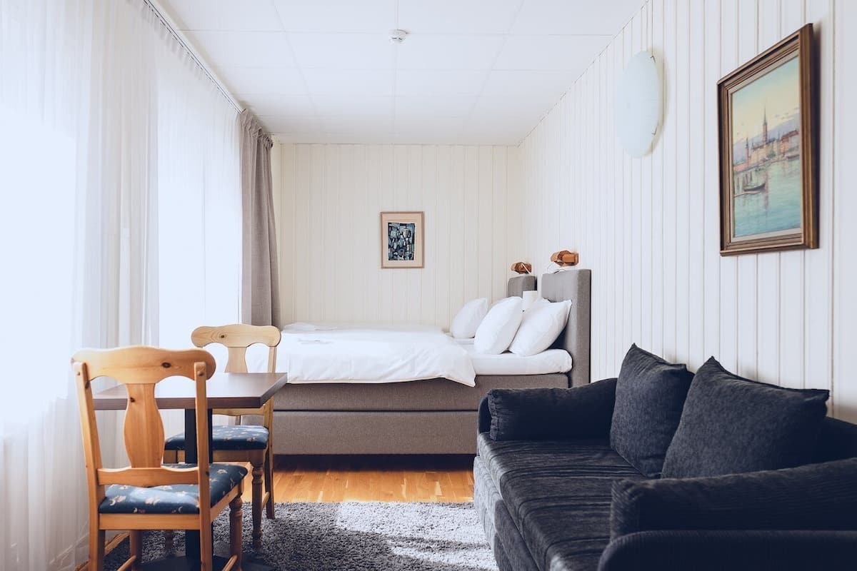 Habitación de hotel con cama, sofá, sillón, mesita y un cuadro en la pared.