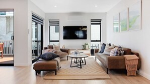 A modern living room with a sofa set, a coffee table, and a TV mounted on the wall. - Central Oasis Townhouse with Parking and Air-con (Auckland Central Suburbs)