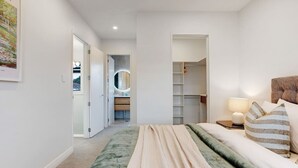 A modern bedroom with a large bed, a walk-in closet, and a bathroom with a circular mirror. - Central Oasis Townhouse with Parking and Air-con (Auckland Central Suburbs)