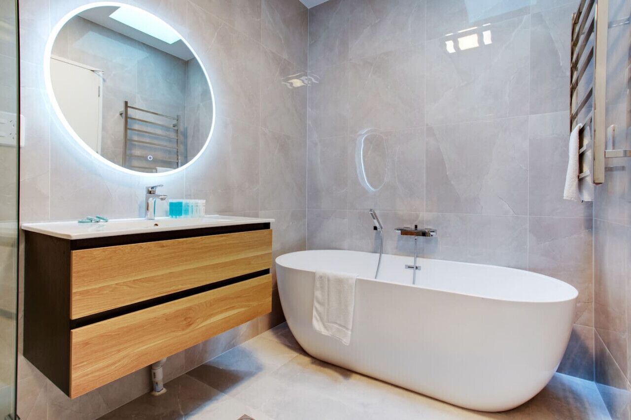 A modern bathroom with a freestanding bathtub, a round mirror, and a wooden vanity.