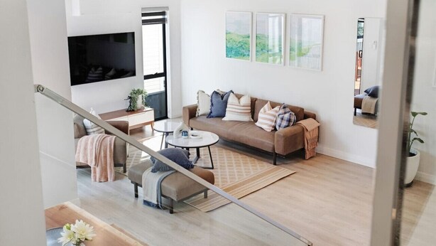 A modern living room with a sofa, coffee table, and a TV mounted on the wall. - Central Oasis Townhouse with Parking and Air-con (Auckland Central Suburbs)