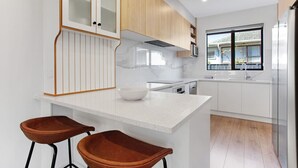 A modern kitchen with white cabinetry, a marble countertop, two brown bar stools, and a window providing a view of the outside. - Central Oasis Townhouse with Parking and Air-con (Auckland Central Suburbs)