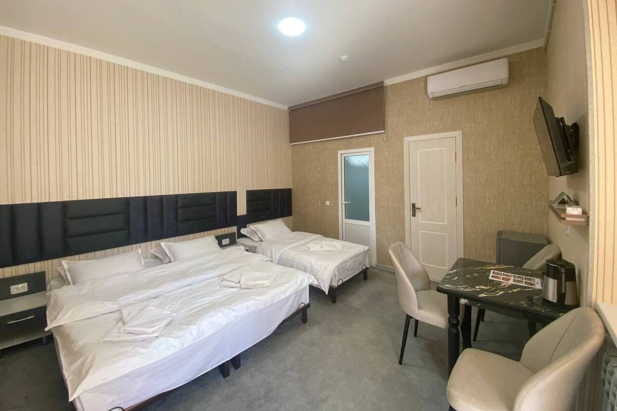 A hotel room with two beds, a desk, a chair, a TV, and an air conditioning unit.
