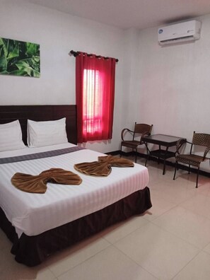 Een hotelkamer met een bed, twee stoelen, een klein tafeltje, een rood gordijn en een airconditioning.