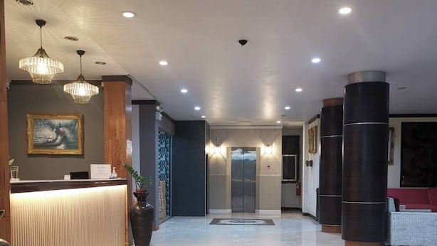 A hotel reception area with a reception desk, a welcome mat, and a hallway leading to elevators. - PS Hotel Saraburi (Phra Phutthabat)