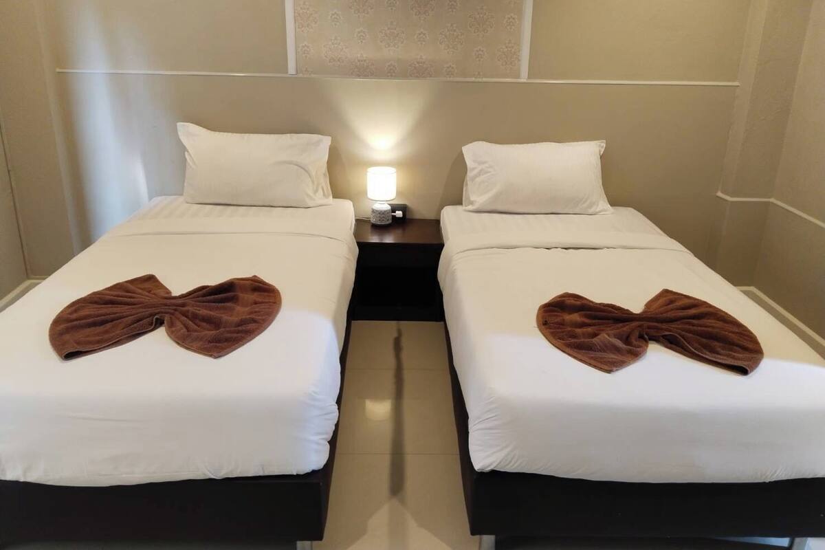 A hotel room with two beds, each with white bedding and a brown towel on the bed. There is a nightstand between the beds with a lamp on it.