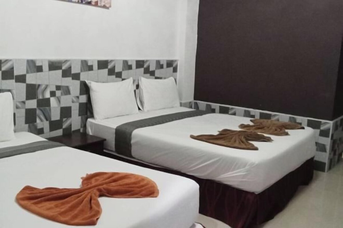A hotel room with two beds, each with white linens and a brown blanket. The room has a modern design with a checkered pattern on the headboard and a dark accent wall.
