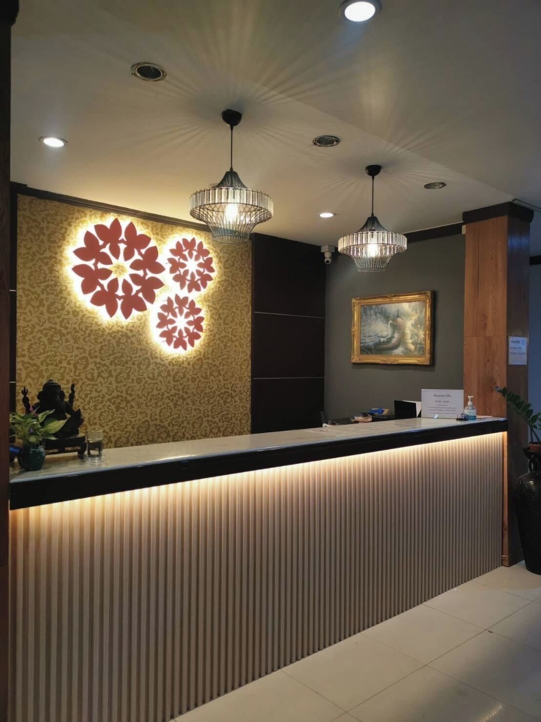 A reception area with a modern design, featuring a decorative wall with illuminated floral patterns, a reception desk with a built-in light, and pendant lighting above.