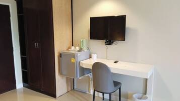 Una habitación compacta con kitchenette, un escritorio, una silla, un televisor y un armario.
