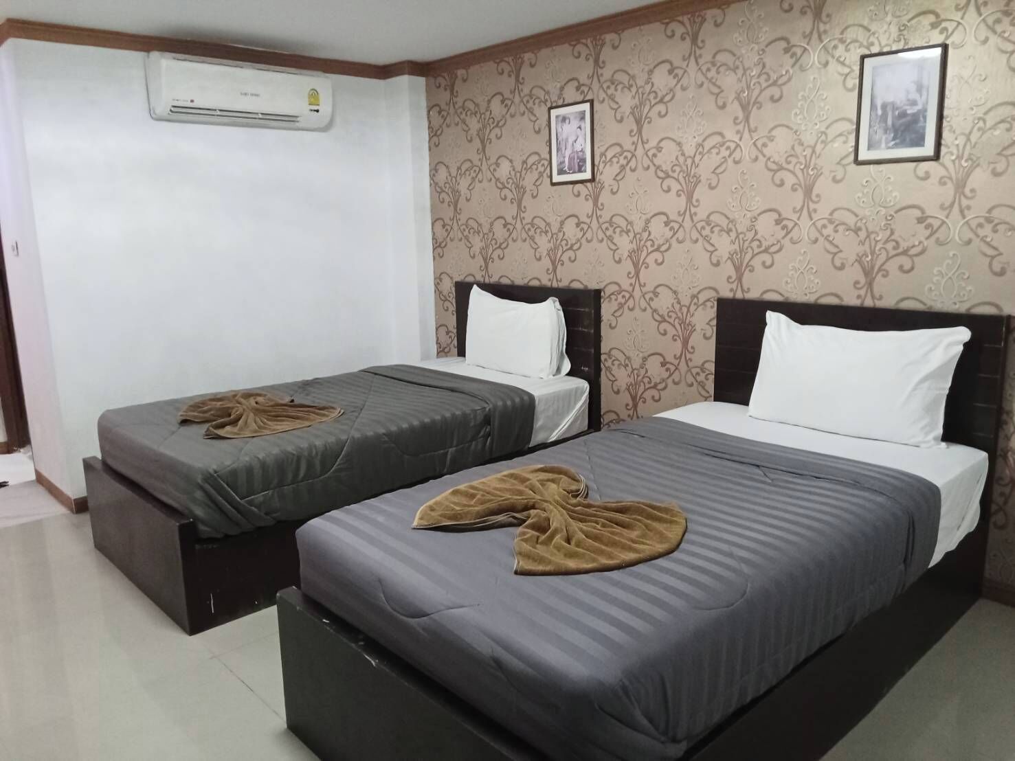 Habitación de hotel con dos camas, un armario, un equipo de aire acondicionado y papel tapiz estampado.