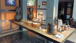 A breakfast bar with various food items and condiments, framed artwork on the walls, and a modern interior design. - PS Hotel Saraburi (Phra Phutthabat)