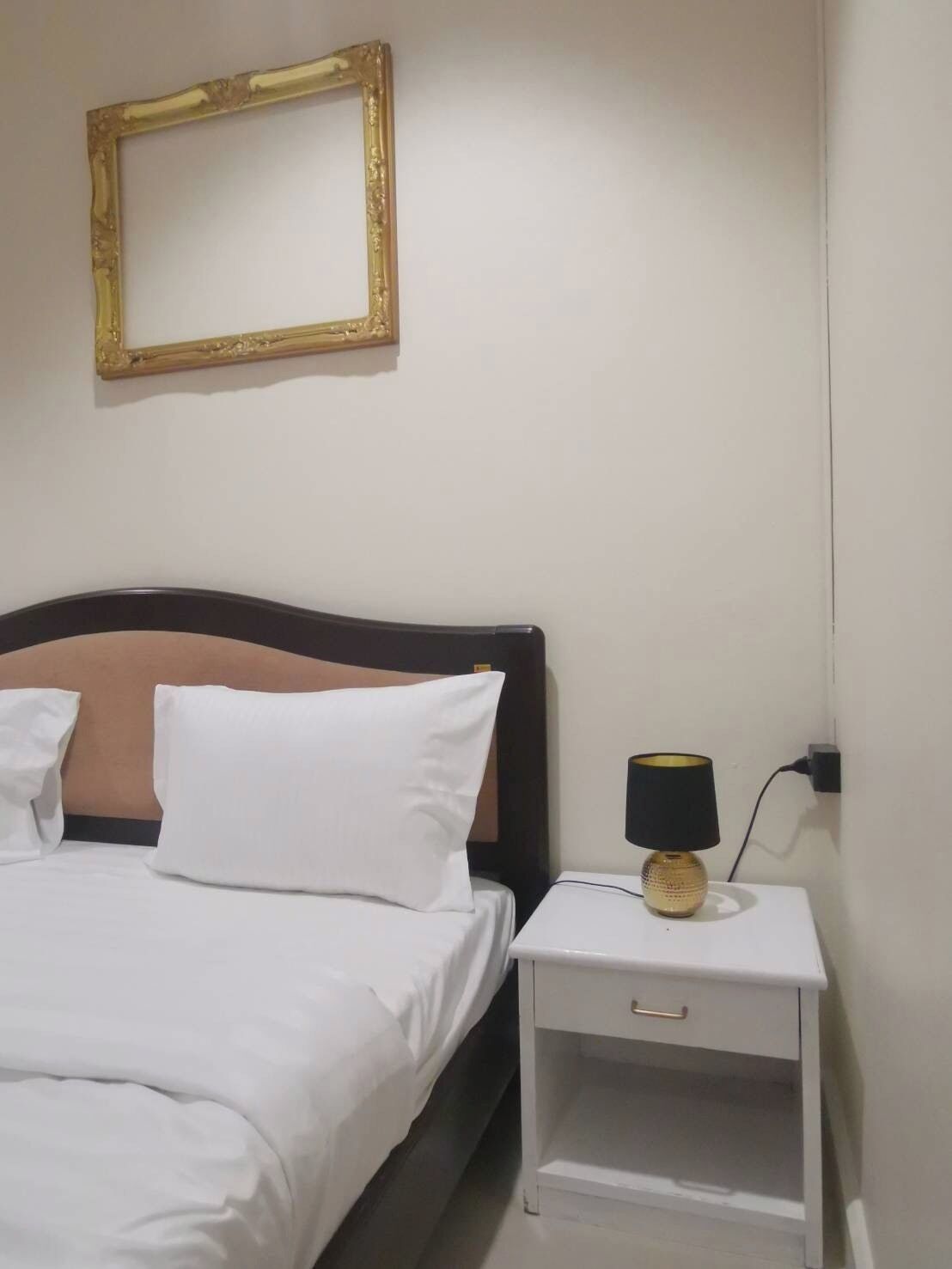 Una cama bien tendida con ropa blanca, un cabecero de madera y una mesita de noche con una lámpara.